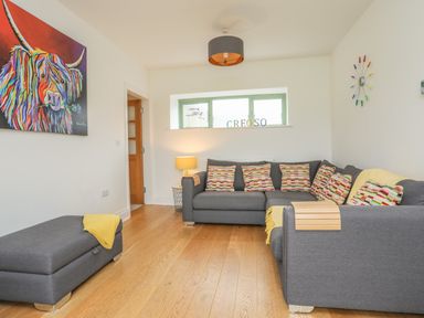 A living room with a gray sectional sofa and a matching ottoman with colorful cushions and a yellow throw at Mynydd Parys in Brynsiencyn