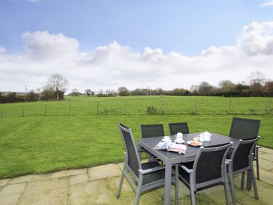 An outdoor patio with a dining table and six chairs overlooking a grassy fenced field at Mynydd Parys in Brynsiencyn