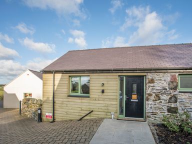 Exterior view of a semi detached house with wood and stone walls a black front door and a paved driveway at Mynydd Parys in Brynsiencyn