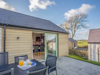 An outdoor patio area with a table set with a jug of orange juice and tea set outside a building with sliding glass doors at Mynydd Parys in Brynsiencyn