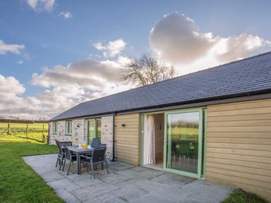 An outdoor patio area with a table and six chairs beside a house with stone and wood siding at Mynydd Parys in Brynsiencyn