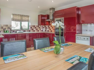 A kitchen with red cabinets a wooden table with place mats and a flower vase at Mynydd Parys in Brynsiencyn