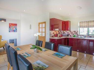 A dining table with six black chairs and a flower vase in a kitchen with red cabinets at Mynydd Parys in Brynsiencyn