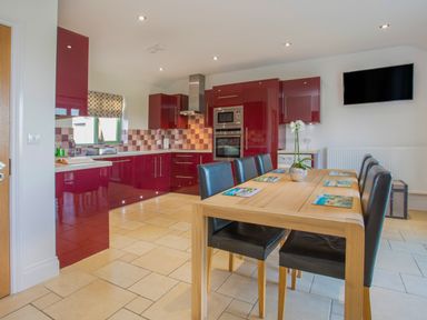 A kitchen with red cabinets a wooden dining table with black chairs and a wall-mounted TV at Mynydd Parys in Brynsiencyn