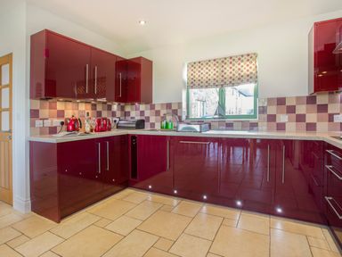 A kitchen with red cabinets beige tiled floor and a window with a patterned blind at Mynydd Parys in Brynsiencyn