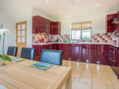 A kitchen with burgundy cabinets and a wooden dining table with black chairs at Mynydd Parys in Brynsiencyn