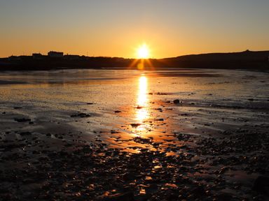 A sunset over a rocky beach with houses in the distance at Pant yr Hyman in Rhoscolyn