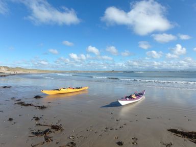 Two kayaks on a sandy beach near the sea with people walking in the distance at Pant yr Hyman in Rhoscolyn