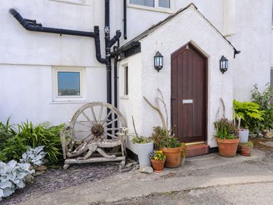 An entrance door with potted plants and an old wooden wagon wheel bench outside at Pant yr Hyman in Rhoscolyn