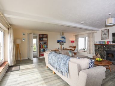 A living room with beige sofas a blue checkered throw a wooden coffee table and a stone fireplace at Pant yr Hyman in Rhoscolyn