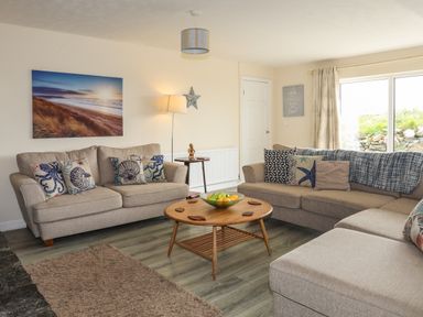 A living room with two beige sofas a wooden coffee table with a bowl of fruit a floor lamp and a large window at Pant yr Hyman in Rhoscolyn