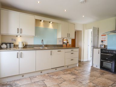 A kitchen with white cabinets a sink a kettle and an oven at Pant yr Hyman in Rhoscolyn
