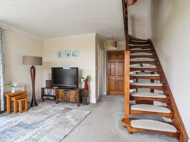 A living room with a television on a wooden stand a floor lamp nested tables and wooden stairs at Pant yr Hyman in Rhoscolyn