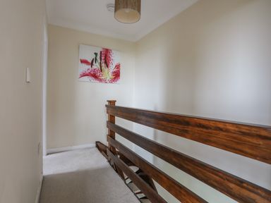 A hallway with beige walls a wooden railing a light fixture and a flower painting at Pant yr Hyman in Rhoscolyn