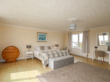A bedroom with a bed nightstands lamps a round wooden table a chair a dressing table with a mirror and a window at Pant yr Hyman in Rhoscolyn