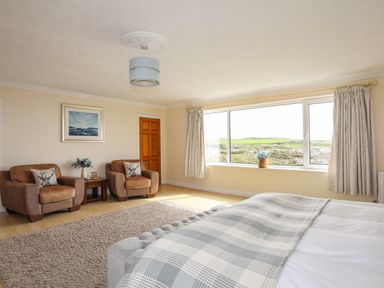 A bedroom with two armchairs a side table and a large window showing a landscape at Pant yr Hyman in Rhoscolyn