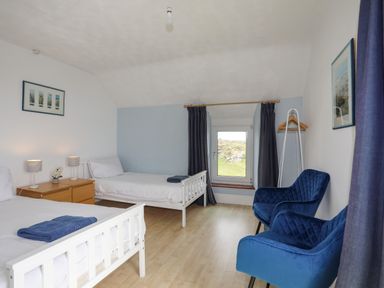A bedroom with two single beds bedside table two blue chairs and a window at Pant yr Hyman in Rhoscolyn