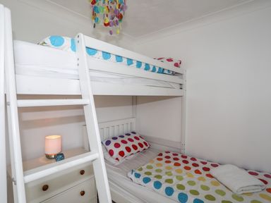 A bedroom with a white bunk bed and a nightstand with a lamp and an ornament at Pant yr Hyman in Rhoscolyn