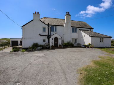 A white two-story house with chimneys and a gravel driveway at Pant yr Hyman in Rhoscolyn