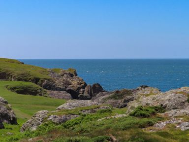 A rocky coastline with green grass and ocean view at Pant yr Hyman in Rhoscolyn