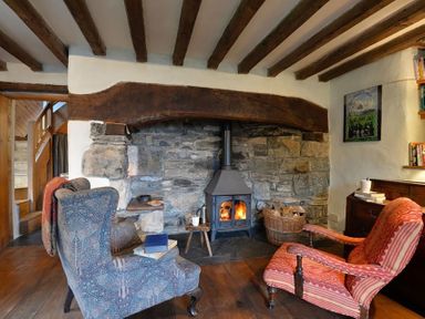 A room with two armchairs a wood burning stove and a basket of firewood at Pantlleni in Nant Gwynant