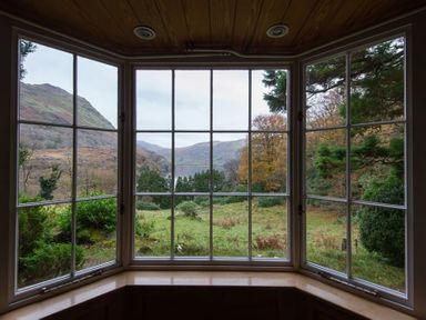 A window with multiple panes overlooking a grassy landscape with trees and hills at Pantlleni in Nant Gwynant