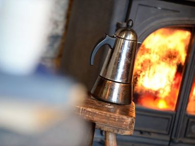 A metal coffee pot on a wooden stool in front of a burning fireplace at Pantlleni in Nant Gwynant