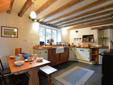 A kitchen with wooden beams on the ceiling a wooden table set with bowls mugs and a teapot at Pantlleni in Nant Gwynant