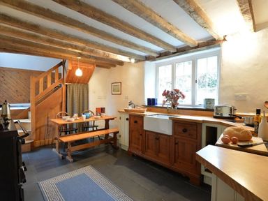 A kitchen with wooden cabinets a farmhouse sink a wooden dining table and stairs in Pantlleni in Nant Gwynant