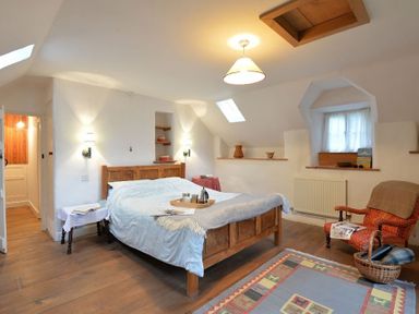 A bedroom with a wooden bed and armchair with a book basket on a rug at Pantlleni in Nant Gwynant