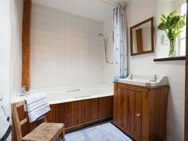 A bathroom with a bathtub shower wooden cabinet and chair with a towel at Pantlleni in Nant Gwynant