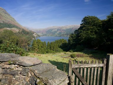 A landscape with a stone wall and wooden gate overlooking a lake surrounded by trees and hills at Pantlleni in Nant Gwynant