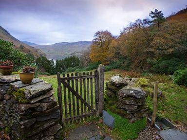 A garden gate opening to a grassy area with trees and a lake in the background at Pantlleni in Nant Gwynant