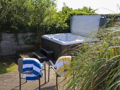 An outdoor area with a hot tub, two chairs with towels, and surrounding greenery at Pencraig in Trearddur Bay