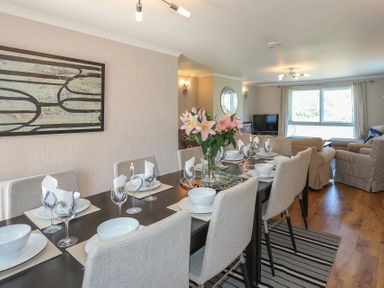 A dining area with a set table and a seating area with sofas and a television at Pencraig in Trearddur Bay