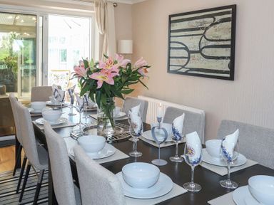 A dining room with a table set with plates bowls glasses a vase of flowers and a candle at Pencraig in Trearddur Bay
