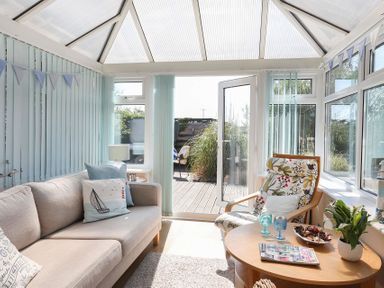A conservatory with a beige sofa a floral armchair a round wooden table and glass doors leading outside at Pencraig in Trearddur Bay