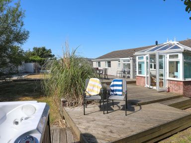 A wooden deck with two chairs and a conservatory attached to a single story house at Pencraig in Trearddur Bay