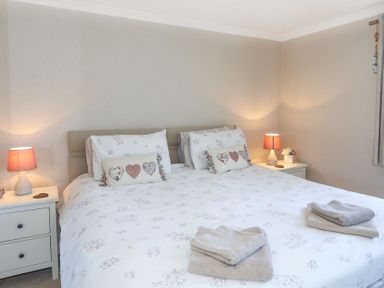 A bedroom with a bed two bedside tables with lamps and folded towels on the bed at Pencraig in Trearddur Bay