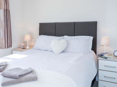 A bedroom with a bed between two nightstands with lamps and folded towels at Pencraig in Trearddur Bay