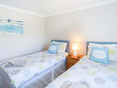 A bedroom with two single beds bedside table with lamp and towel on one bed at Pencraig in Trearddur Bay