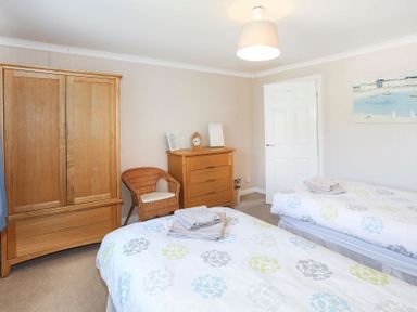 A bedroom with two single beds a wooden wardrobe a chest of drawers and a wicker chair at Pencraig in Trearddur Bay