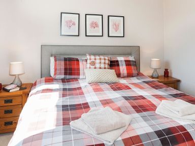 A bedroom with a bed with red plaid bedding and two bedside tables with lamps at Pencraig in Trearddur Bay