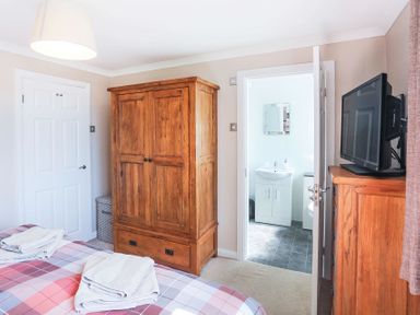 A bedroom with a bed and folded towels a wooden wardrobe a chest of drawers with a TV and a door leading to a bathroom at Pencraig in Trearddur Bay