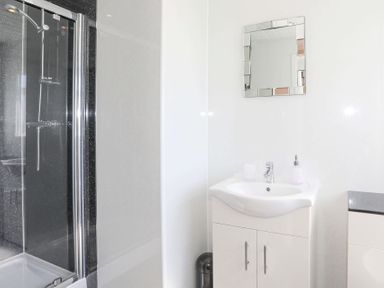 A bathroom with a shower enclosure a white sink with cabinet a mirror above it and a soap dispenser at Pencraig in Trearddur Bay