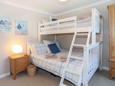 A bedroom with a white bunk bed wooden nightstand with a lamp and a basket on the floor at Pencraig in Trearddur Bay