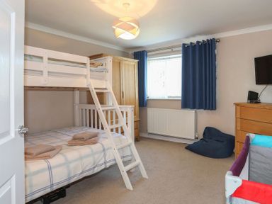 A bedroom with a white bunk bed blue curtains wooden wardrobe and chest of drawers at Pencraig in Trearddur Bay