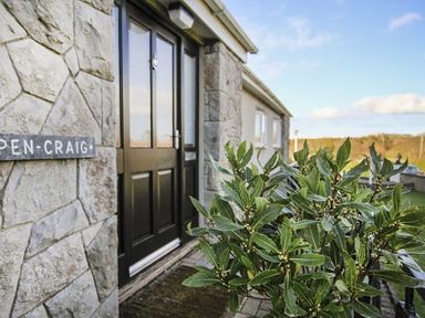 The entrance of a stone house with a black door and a green bush near the door at Pencraig in Trearddur Bay