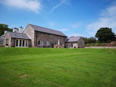 A stone house with multiple windows and patio furniture on a lawn at Penrhyn Barn in Dulas