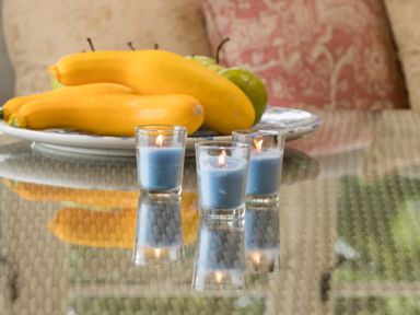 A glass table with three lit blue candles and a plate of yellow squash and green apples in a room at Penrhyn Barn in Dulas